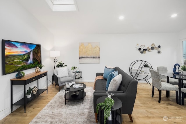 living room with vaulted ceiling with skylight and light hardwood / wood-style flooring