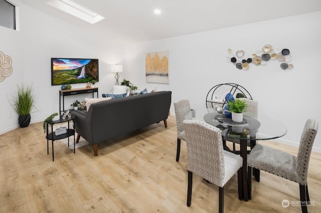 dining area featuring lofted ceiling with skylight and light hardwood / wood-style floors