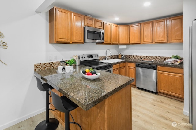 kitchen with stainless steel appliances, sink, light wood-type flooring, and kitchen peninsula