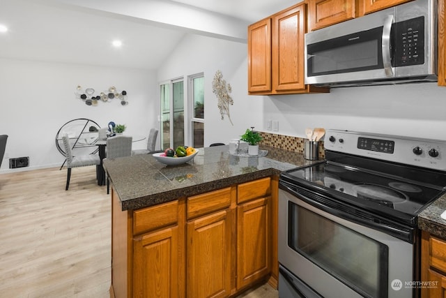 kitchen featuring stainless steel appliances, vaulted ceiling, kitchen peninsula, and light hardwood / wood-style flooring