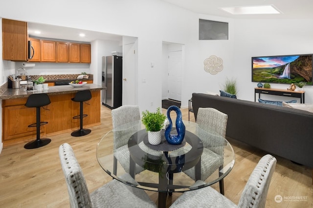 dining area featuring sink, a towering ceiling, a skylight, and light hardwood / wood-style floors