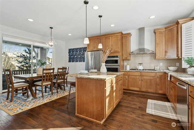 kitchen with stainless steel appliances, wall chimney range hood, a center island, dark wood-style floors, and decorative light fixtures