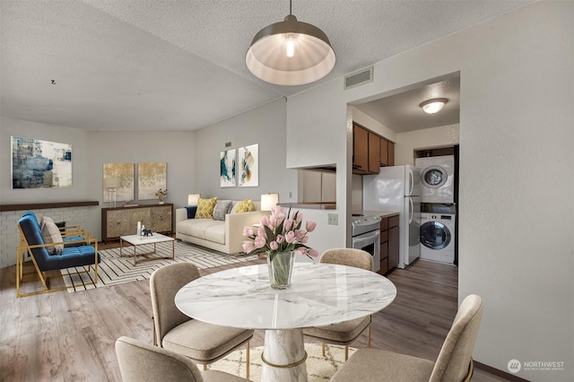 dining space with stacked washer / dryer, a textured ceiling, and light hardwood / wood-style flooring