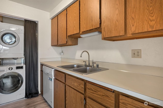 laundry area with stacked washer / drying machine, light hardwood / wood-style floors, and sink