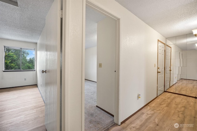 hallway with a textured ceiling and light wood-type flooring