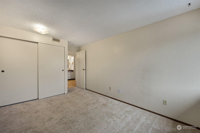 unfurnished bedroom with light carpet, a textured ceiling, and a closet