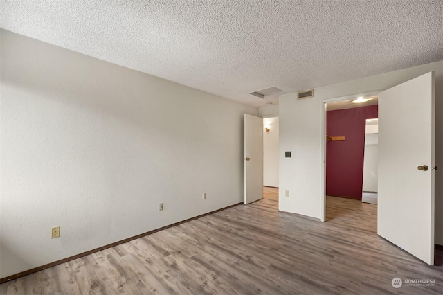 unfurnished bedroom featuring hardwood / wood-style flooring, a walk in closet, a closet, and a textured ceiling