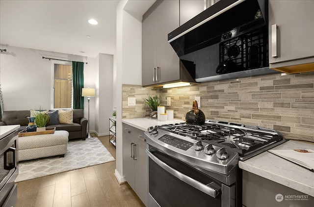 kitchen with stainless steel gas range, light hardwood / wood-style flooring, gray cabinetry, decorative backsplash, and exhaust hood