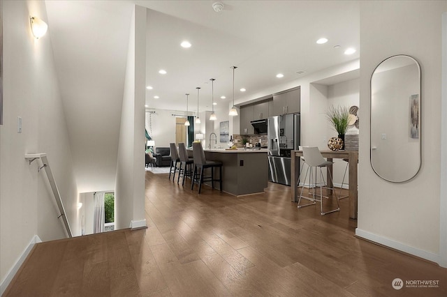 kitchen with dark wood-type flooring, stainless steel fridge, a kitchen breakfast bar, a kitchen island with sink, and backsplash