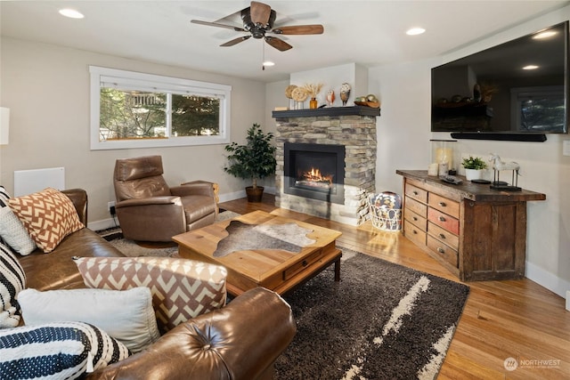 living room with a stone fireplace, light hardwood / wood-style flooring, and ceiling fan