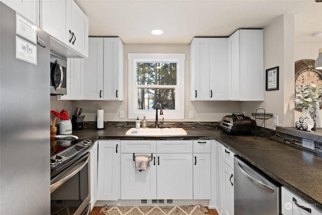 kitchen with white cabinetry, stainless steel appliances, sink, and dark stone counters