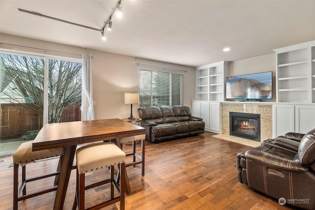 living area with a healthy amount of sunlight, built in shelves, a tiled fireplace, and wood finished floors