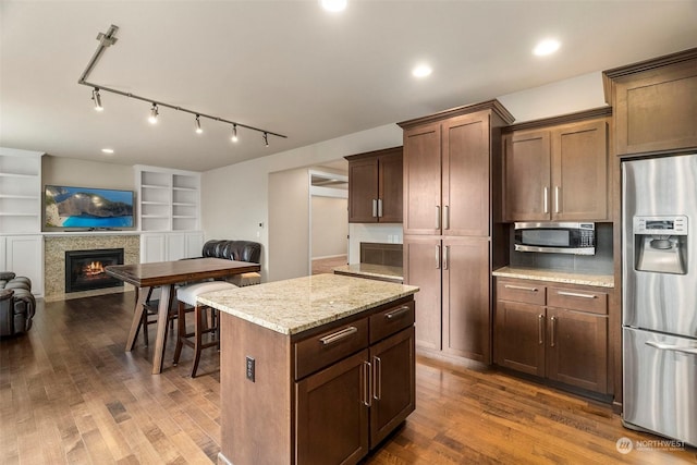 kitchen featuring dark wood-style floors, a fireplace with flush hearth, appliances with stainless steel finishes, open floor plan, and light stone counters