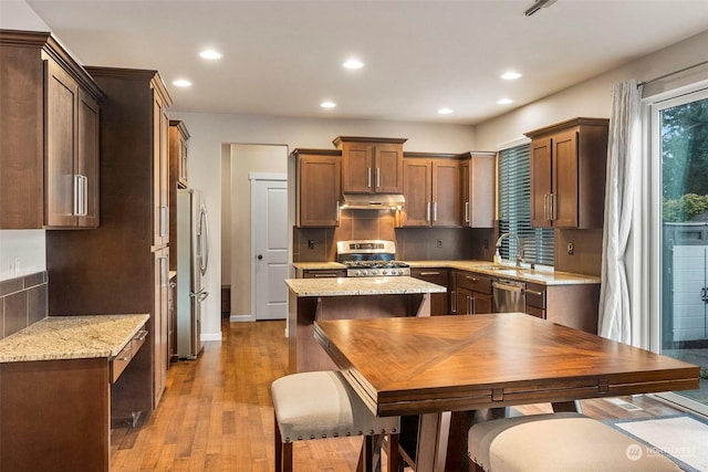 kitchen featuring tasteful backsplash, light wood-style flooring, light stone countertops, stainless steel appliances, and a sink