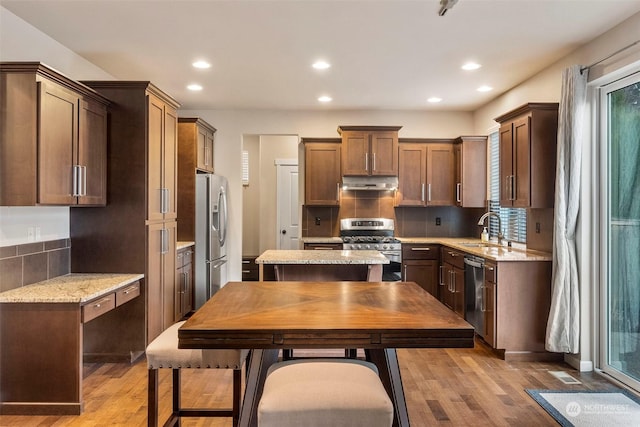 kitchen with appliances with stainless steel finishes, light wood-style floors, a sink, light stone countertops, and under cabinet range hood