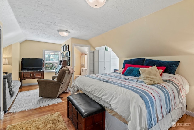 bedroom featuring lofted ceiling, connected bathroom, light hardwood / wood-style floors, and a textured ceiling