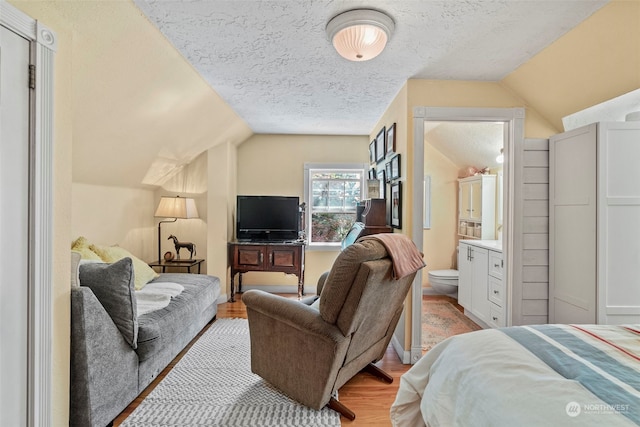 bedroom featuring ensuite bathroom, light hardwood / wood-style floors, vaulted ceiling, and a textured ceiling