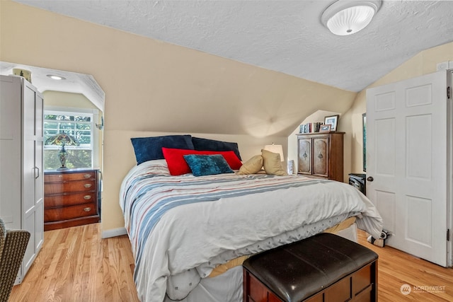 bedroom featuring vaulted ceiling, a textured ceiling, and light wood-type flooring