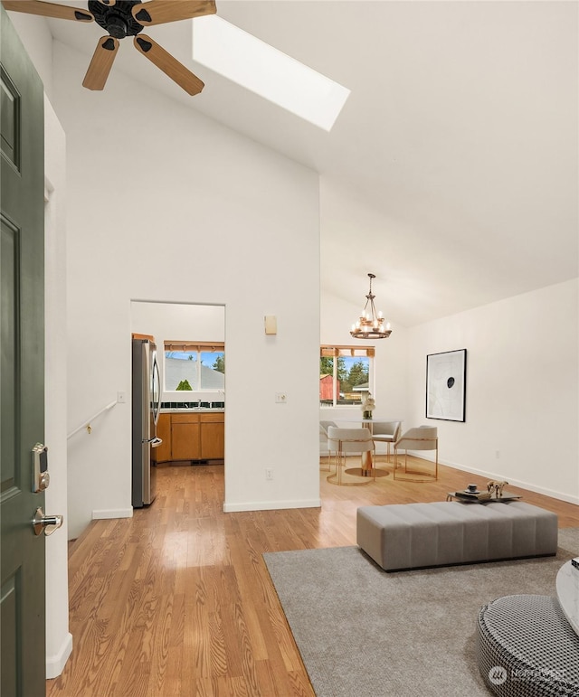 living room with a skylight, ceiling fan with notable chandelier, high vaulted ceiling, and light hardwood / wood-style flooring