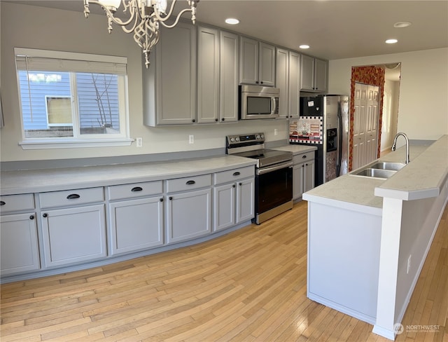 kitchen with sink, an inviting chandelier, gray cabinets, stainless steel appliances, and light hardwood / wood-style floors