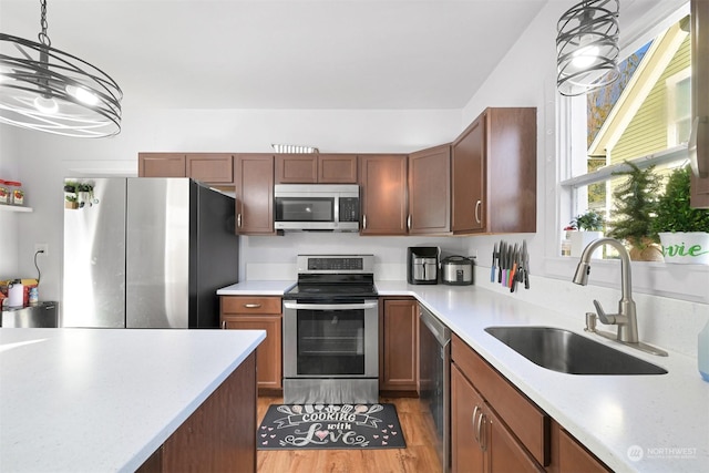 kitchen featuring sink, stainless steel appliances, hanging light fixtures, and light wood-type flooring