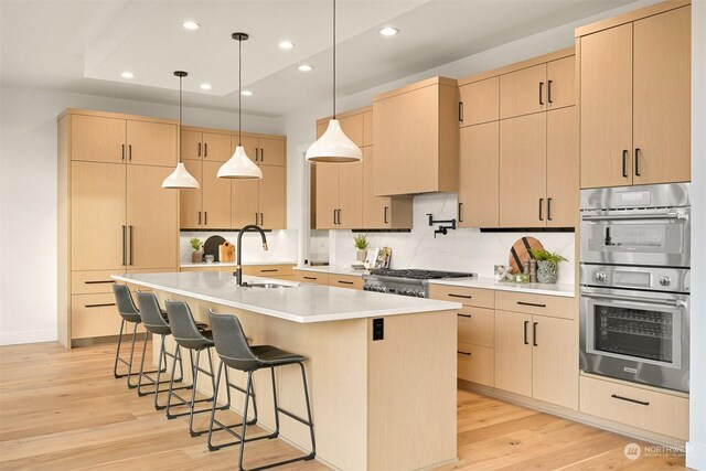 kitchen with double oven, an island with sink, light brown cabinetry, and sink