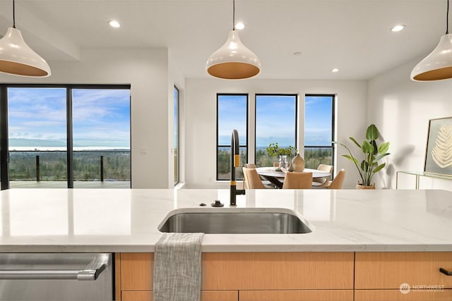 kitchen featuring light brown cabinetry, light stone countertops, sink, and hanging light fixtures