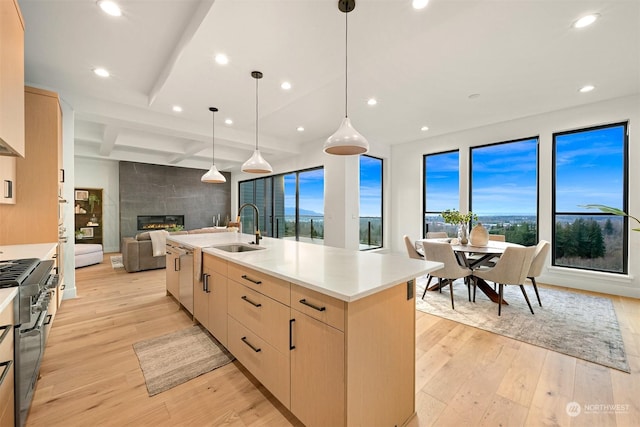 kitchen featuring hanging light fixtures, sink, a center island with sink, and light brown cabinetry