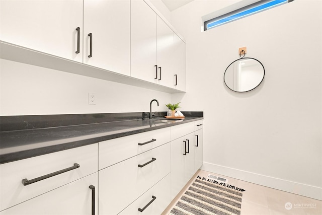 bar featuring sink, light tile patterned floors, and white cabinets