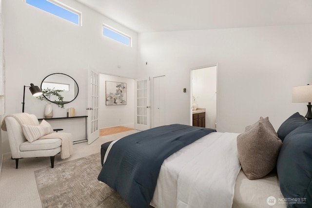 bedroom with french doors, light colored carpet, a towering ceiling, and ensuite bathroom