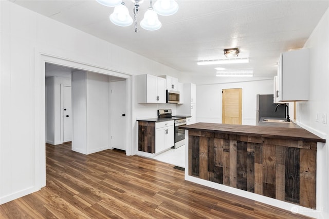 kitchen with appliances with stainless steel finishes, sink, white cabinets, dark hardwood / wood-style flooring, and kitchen peninsula