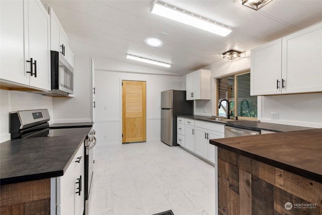 kitchen with stainless steel appliances, butcher block counters, sink, and white cabinets