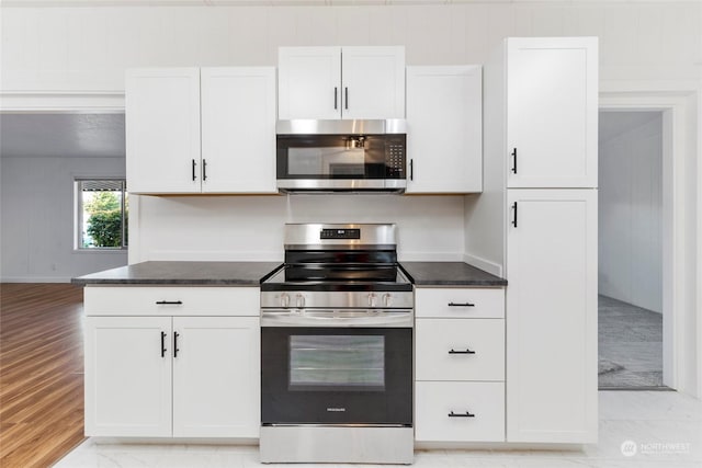 kitchen with white cabinetry, stainless steel appliances, light hardwood / wood-style floors, and dark stone countertops