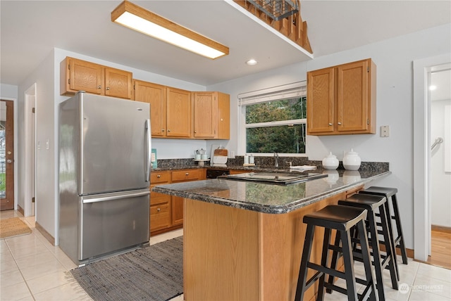 kitchen featuring light tile patterned floors, stainless steel fridge, kitchen peninsula, and dark stone counters