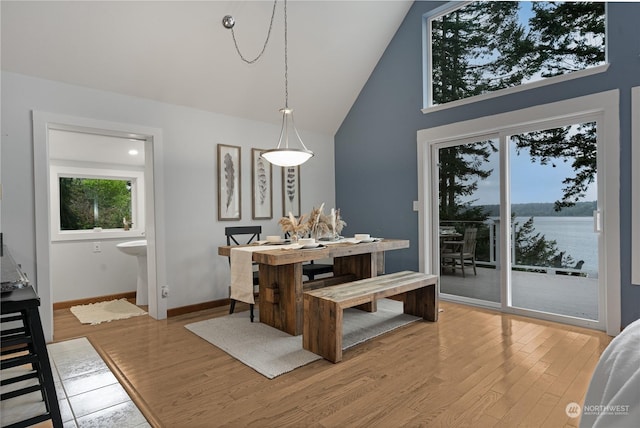 dining area with a water view, high vaulted ceiling, and light hardwood / wood-style floors