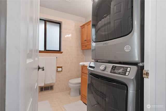 bathroom featuring stacked washer / drying machine, toilet, tile patterned flooring, and tile walls