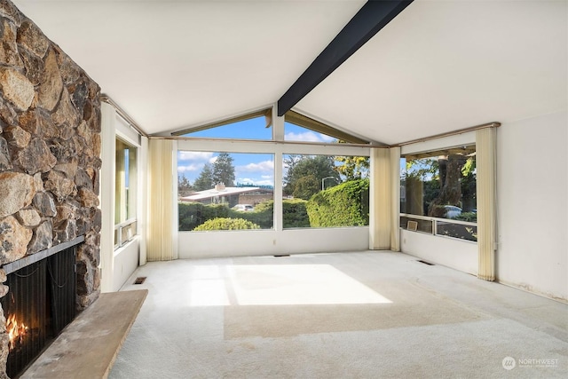 unfurnished sunroom featuring a stone fireplace and lofted ceiling with beams