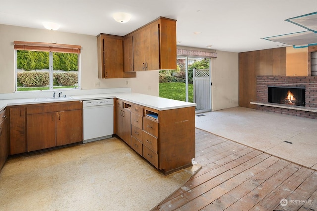 kitchen with sink, a brick fireplace, light wood-type flooring, white dishwasher, and kitchen peninsula