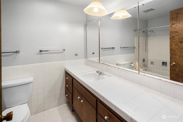 full bathroom featuring vanity, toilet, tiled shower / bath combo, and tile walls