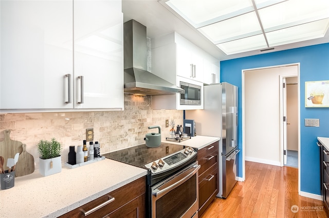 kitchen featuring white cabinetry, stainless steel appliances, dark brown cabinetry, decorative backsplash, and wall chimney exhaust hood