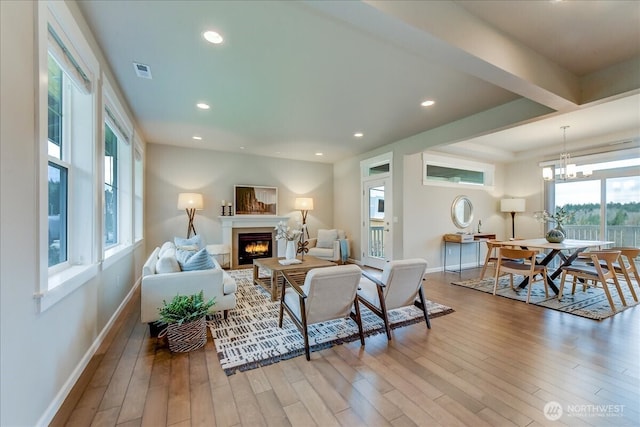 living area featuring visible vents, baseboards, recessed lighting, a warm lit fireplace, and light wood-style floors