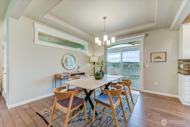 dining space featuring light wood-type flooring, a tray ceiling, and baseboards