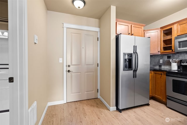 kitchen with tasteful backsplash, stainless steel appliances, light hardwood / wood-style floors, and dark stone countertops