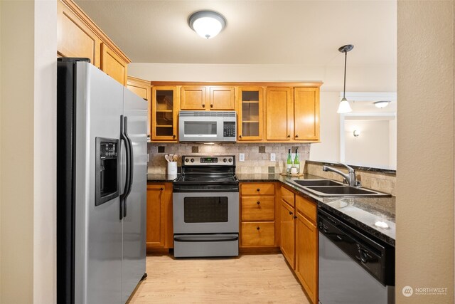 kitchen featuring appliances with stainless steel finishes, decorative light fixtures, sink, backsplash, and light wood-type flooring