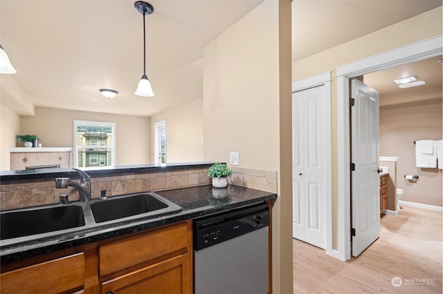 kitchen featuring sink, dark stone countertops, hanging light fixtures, light hardwood / wood-style floors, and stainless steel dishwasher