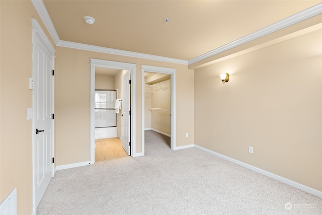 unfurnished bedroom with ensuite bathroom, a walk in closet, crown molding, light carpet, and a closet