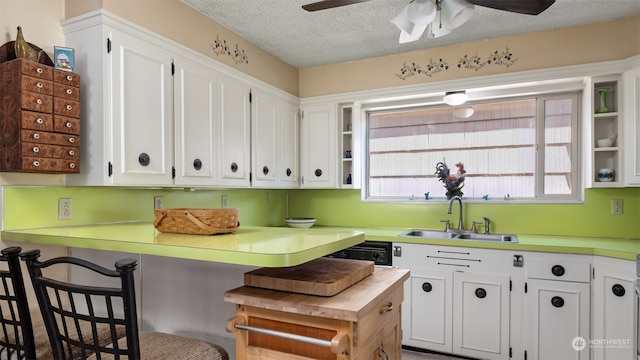 kitchen with sink, ceiling fan, a kitchen bar, a textured ceiling, and white cabinets