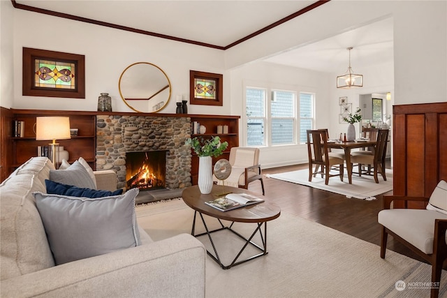 living room featuring wood-type flooring, a stone fireplace, an inviting chandelier, and crown molding