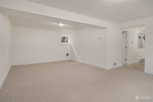 spare room featuring a baseboard radiator, light carpet, and a textured ceiling