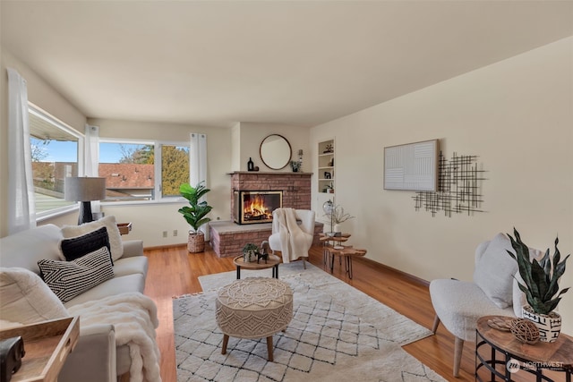 living room with built in shelves, light hardwood / wood-style floors, and a brick fireplace